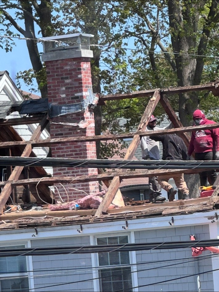 Workers repairing a roof with exposed rafters and a brick chimney