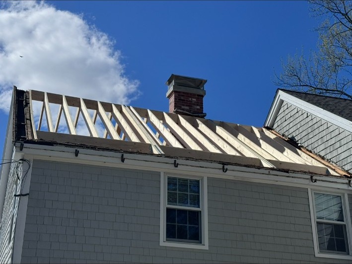 Roof replacement in progress with new rafters and brick chimney